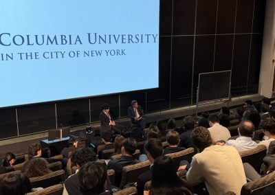 View from the audience of Siyang Ding and Blair Effron on stage beneath the Columbia University in the City of New York screen